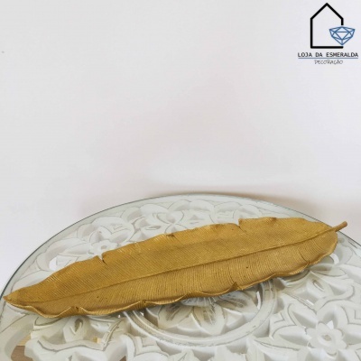 Prato decorativo dourado em forma de folha sobre superfície branca com padrão floral