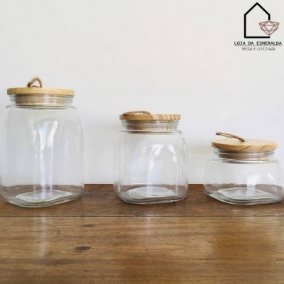 Três frascos de vidro com tampas de madeira em diferentes tamanhos sobre uma mesa de madeira.