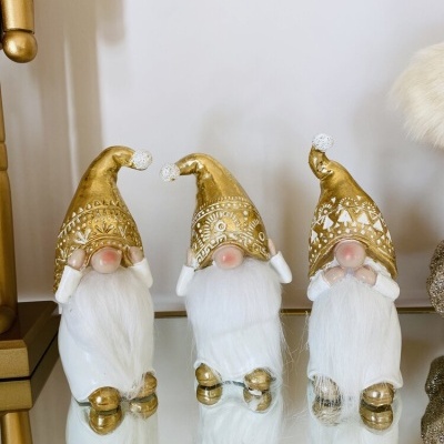 Três duendes decorativos com gorros dourados e barbas brancas em superfície espelhada.