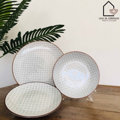 Três pratos com padrão geométrico, bordas castanhas, sobre madeira, planta verde ao fundo