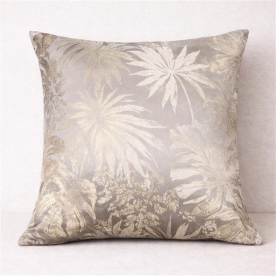 Almofada com padrão de folhas em tons de bege e castanho claro sobre tecido cinza claro