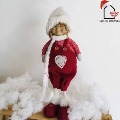 Boneco decorativo natalício com roupa vermelha e bege, chapéu e cachecol branco, botão castanho, sobre madeira e algodão branco