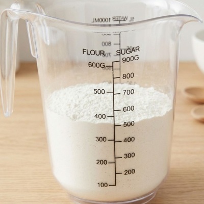 Jarra medidora plástica transparente com farinha branca e marcações de medição