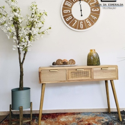 Relógio de parede de madeira, mesa de madeira clara com vaso e planta artificial, tapete colorido, texto LOJA DA ESMERALDA DECORAÇÃO