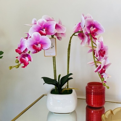 Orquídea artificial rosa em vaso branco sobre mesa com vidro espelhado e estrutura dourada