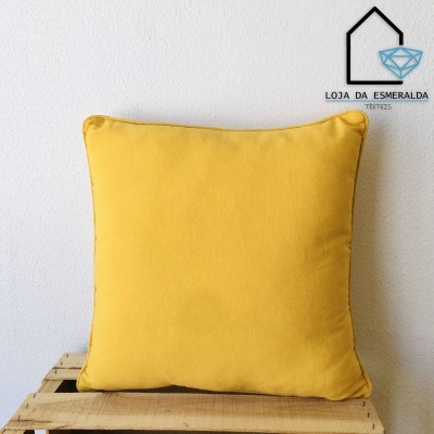 Almofada quadrada amarela sobre superfície de madeira com logótipo da Loja da Esmeralda Têxteis