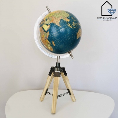 Globo terrestre azul e verde com suporte metálico e base tripé em madeira sobre mesa branca