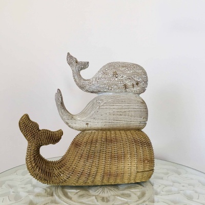 Esculturas empilhadas de baleias feitas de vime e madeira com detalhes decorativos sobre mesa de vidro.