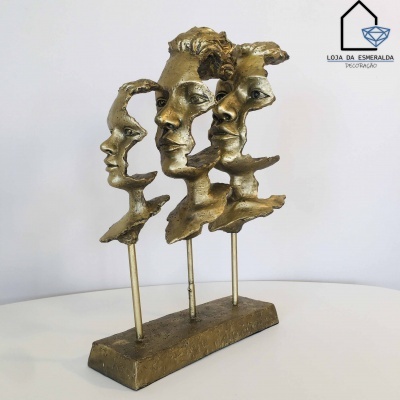 Escultura de três rostos humanos em bronze sobre base retangular com logótipo ao fundo