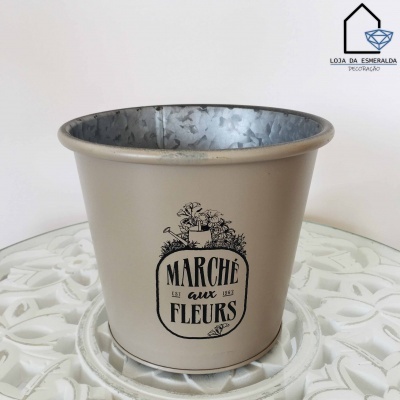Vaso de metal bege com texto e ilustração de flores em mesa branca decorativa