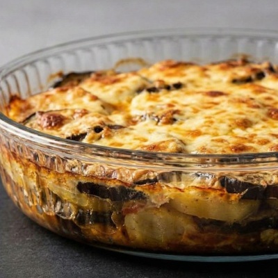 Lasanha de beringela com batata e queijo gratinado em prato de vidro redondo.