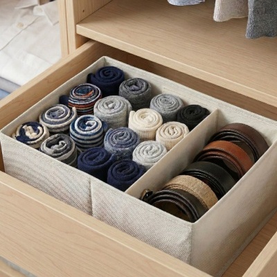 Gaveta aberta com organizador de tecido contendo meias e cintos enrolados.