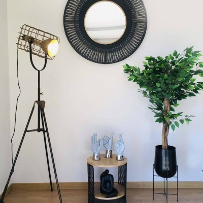 Decoração interior com candeeiro de pé, espelho redondo, mesa com esculturas de mãos e planta em floreira preta