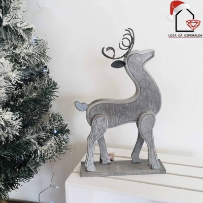 Figurinha decorativa de rena cinzenta em madeira ao lado de árvore de Natal artificial com neve