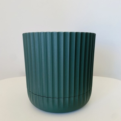 Vaso verde escuro estriado sobre mesa branca.