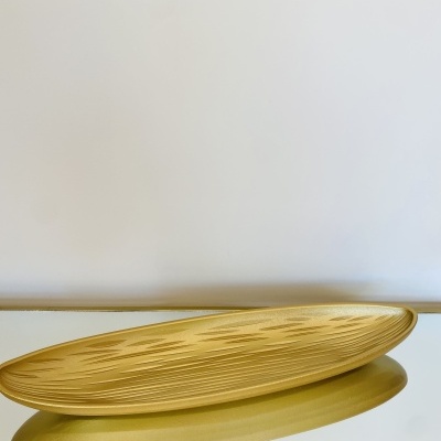 Fruteira dourada oval com relevos geométricos sobre mesa com tampo espelhado e estrutura dourada