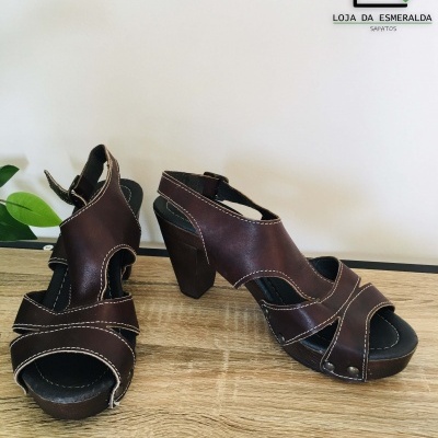 Sapatos femininos de salto alto em pele castanha com costuras claras sobre superfície de madeira