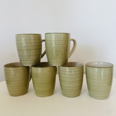Seis chávenas cerâmicas verdes com riscas horizontais finas, duas com asa, dispostas sobre superfície branca
