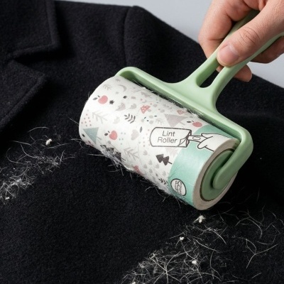 Rolo adesivo verde com texto Lint Roller a limpar pelos brancos de roupa preta
