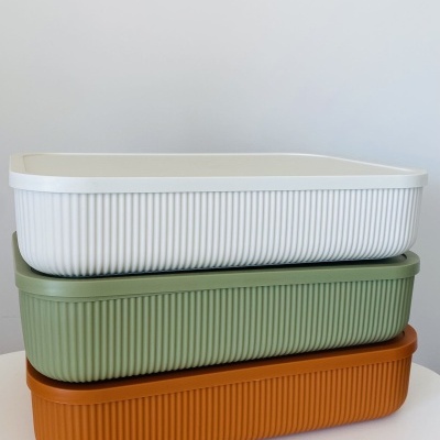 Três caixas retangulares de plástico empilhadas em branco, verde claro e castanho com textura listrada.