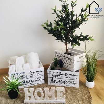 Caixas de madeira brancas decorativas com texto e plantas artificiais, toalhas e garrafas, em tapete de fibra e piso de madeira clara