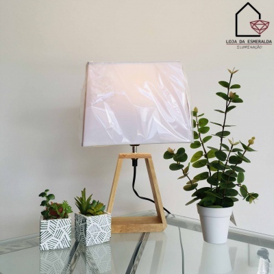 Abajur de madeira com cúpula branca em mesa de vidro com três vasos de plantas verdes