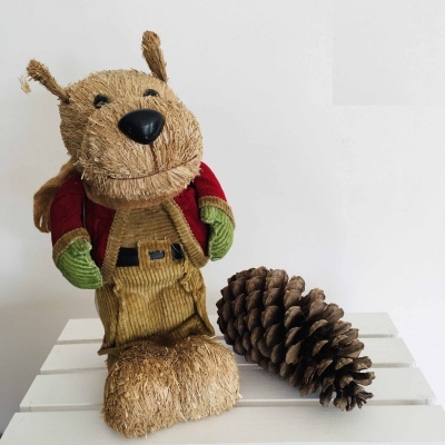 Boneco decorativo de fibra natural em forma de cão com roupa colorida ao lado de pinheiro