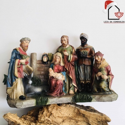 Presépio cerâmico colorido com figuras do Menino Jesus, Maria, São José e três Reis Magos sobre base de madeira.