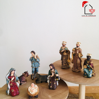 Figuras do presépio em várias cores dispostas em mesas redondas de madeira clara