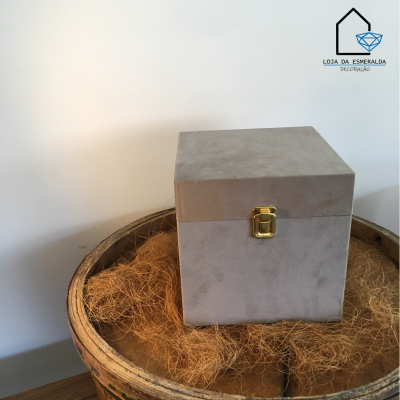 Caixa cinzenta em veludo com fecho dourado sobre recipiente de madeira com palha seca