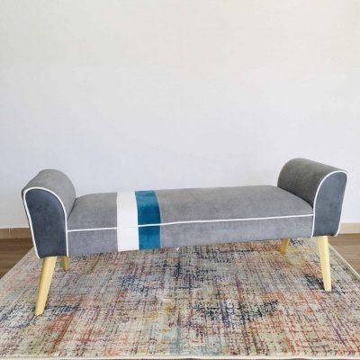 Banco cinzento com riscas e pernas de madeira sobre carpete colorida