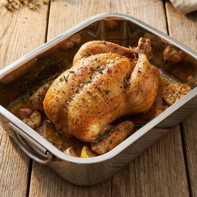 Frango assado temperado em tabuleiro metálico sobre mesa de madeira