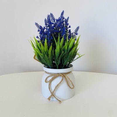 Vaso branco com planta artificial verde e roxa sobre mesa branca