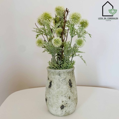 Vaso cinzento com flores artificiais verdes e folhas em mesa branca