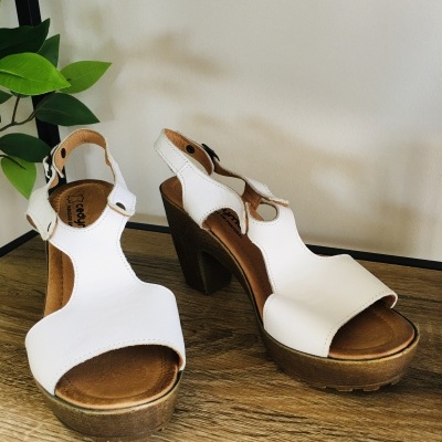 Sapatos de salto alto branco com sola de madeira sobre mesa de madeira