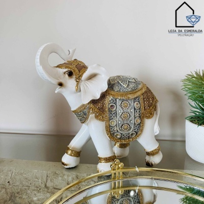 Estatueta decorativa de elefante branca com detalhes dourados e prateados sobre uma superfície espelhada