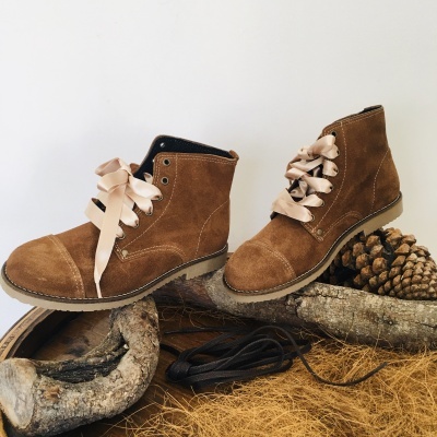 Botas castanhas de camurça com atacadores de fita cor de creme sobre madeira e pinhas