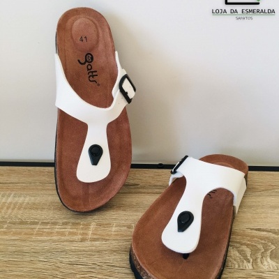 Chinelos de dedo brancos com palmilha castanha e detalhe preto sobre madeira clara