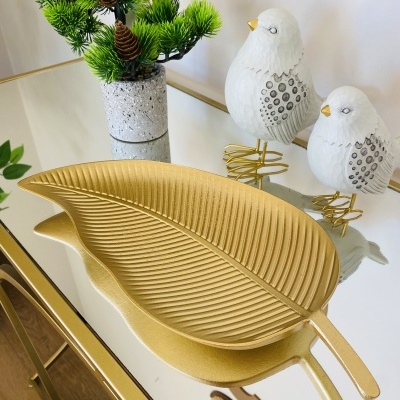 Tabuleiro em forma de folha dourada com pássaros decorativos e planta sobre mesa espelhada