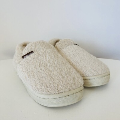 Chinelos felpudos bege claro com sola branca sobre superfície branca