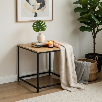 Mesa auxiliar de madeira clara com estrutura preta, decorada com vaso, livros, vela e manta numa sala moderna.