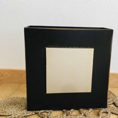 Vaso cerâmico quadrado preto com detalhe creme, sobre tapete rústico e chão de madeira