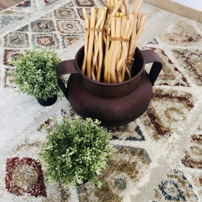 Jarro de metal com ramos de madeira e plantas artificiais sobre tapete geométrico