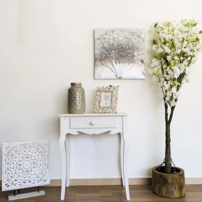 Móvel branco com jarro, moldura, quadro decorativo, painel esculpido e árvore artificial com flores brancas