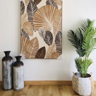 Quadro decorativo de folhas castanhas e pretas com vasos e planta num chão de madeira clara.