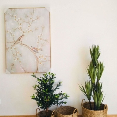 Três cestos trançados com plantas verdes e quadro com pássaros num ambiente interior