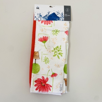 Dois panos de cozinha, um branco com flores vermelhas e outro vermelho liso, embalados