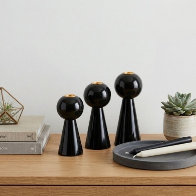 Conjunto de três castiçais pretos brilhantes, velas e planta suculenta sobre mesa de madeira.