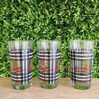Três copos de vidro com padrão xadrez em fundo de plantas verdes