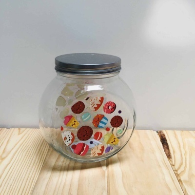 Frasco de vidro redondo decorado com autocolantes coloridos de doces, em superfície de madeira